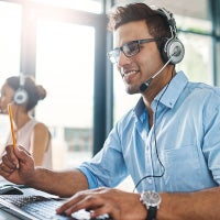 man on headset at office desk, looking at computer