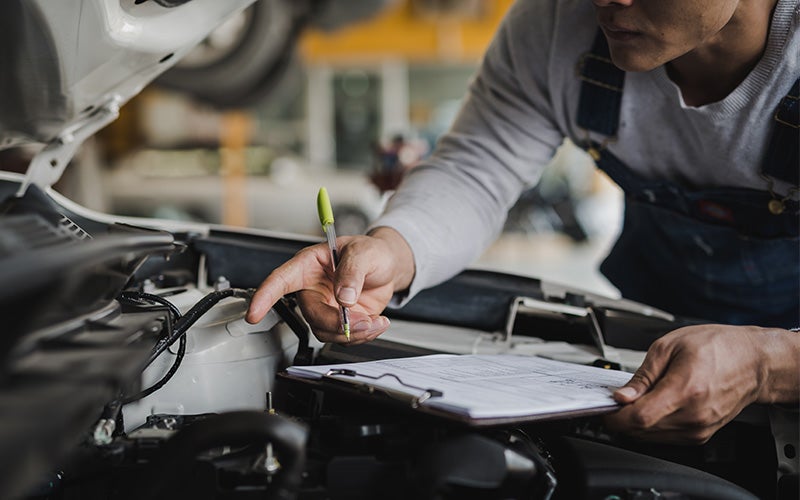 service technician with clipboard, doing an inspection on car's engine