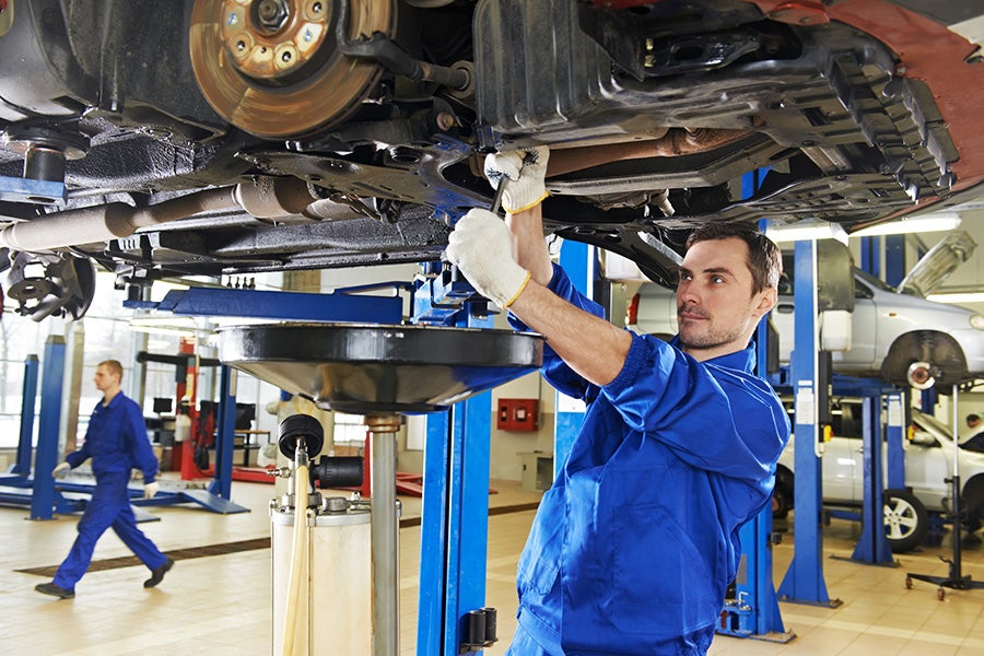 car mechanic performing oil change under a lifted car